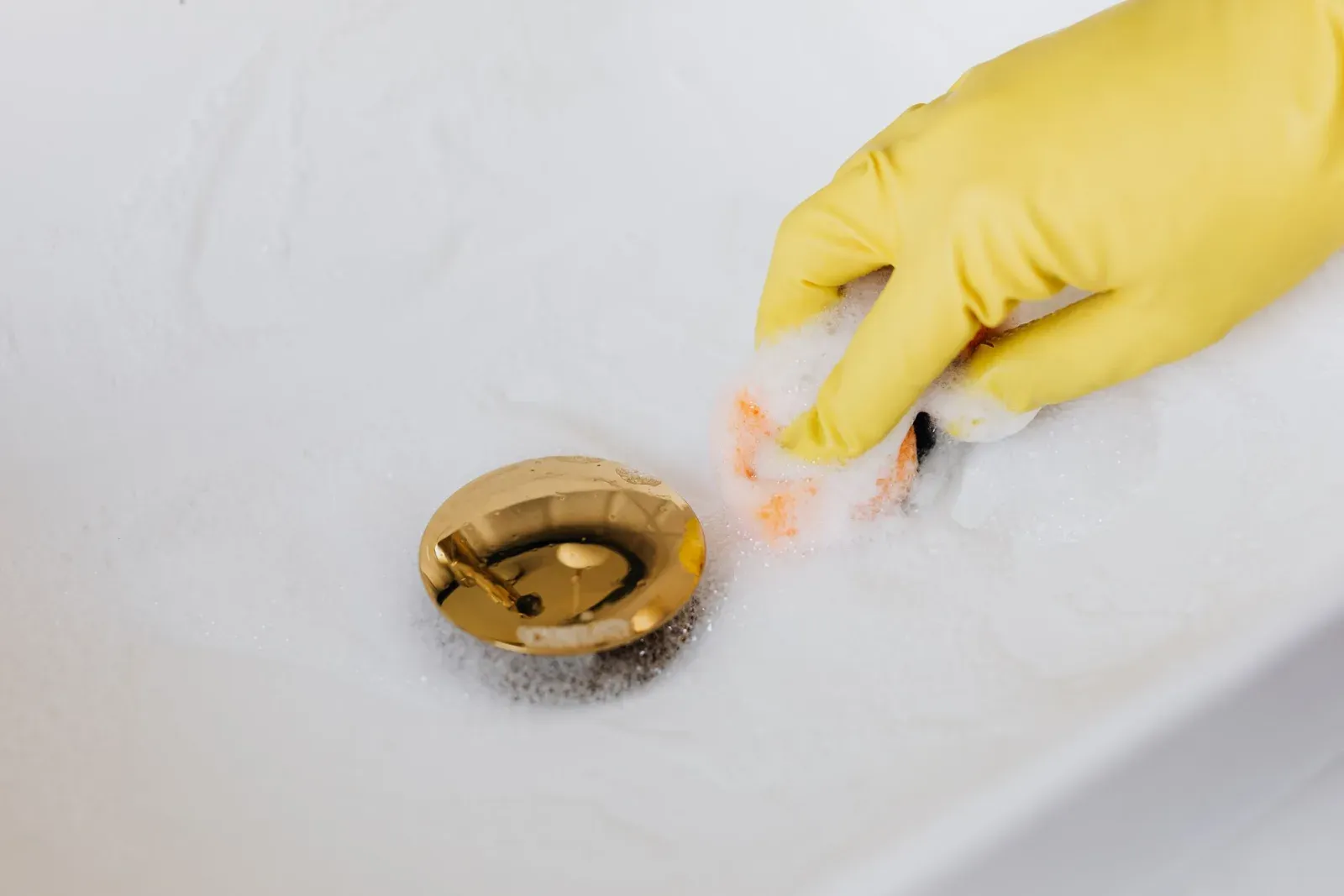 Scrubbing a bathroom sink with a gloved hand