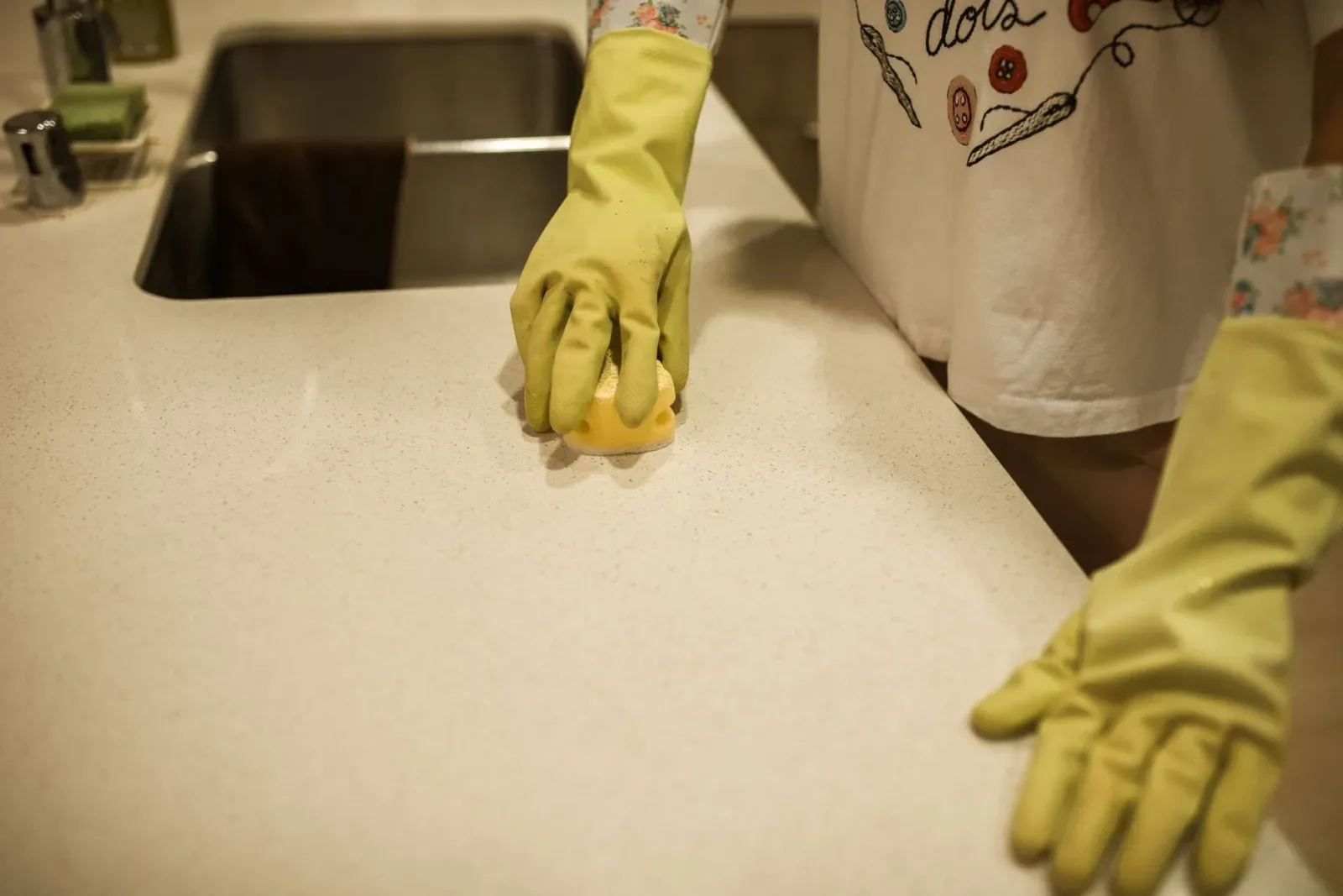 Wiping a kitchen counter with gloves and a sponge